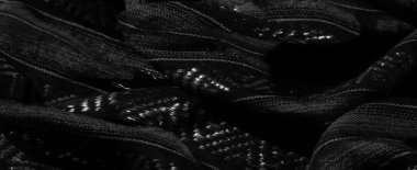 Katlanmış siyah bir kumaşın bulanık görüntüsü, geometrik dokuma desenlerini ve yansıtıcı iplikleri yakalıyor. Karmaşık detaylar ışık ve dokunun etkileşimini vurgular, sofistike bir görünüm yaratır.