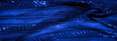 Koyu mavi kumaşın karmaşık kıvrımlarını ve parlak dokularını bulanıklaştırarak yüzeyde parlayan röfleler oluşturarak büyüleyici bir soyut görsel deneyim yaratıyor..