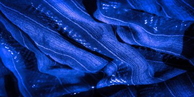 Katlanmış mavi bir kumaşın bulanık görüntüsü ve karmaşık parlak detaylar. İnce gölgeler ve gölgeler, kumaşın dokusunu ve zarafetini gösteren görsel olarak çekici bir kompozisyon oluşturuyor..