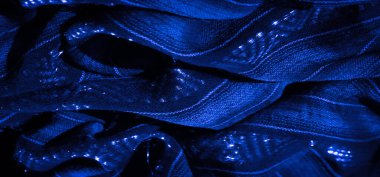 Karmaşık dokuma desenleri ve parıldayan ışık aksanlarıyla akan mavi kumaşın bulanık görüntüsü doku ve derinlik hissi yaratıyor. Katlar ve röfleler dinamik ve soyut bir his ekler..