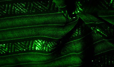 Yeşil ışıkla aydınlatılan katmanlı ve karmaşık desenli yeşil kumaş. Parıltı kumaşın dokusunu vurguluyor. Bu da materyalin içinde organik ve sıvı bir şekil ortaya çıkarıyor..
