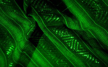 Geometrik desenlerle örülmüş yeşil kumaş kıvrımlarını bulanıklaştırır. Parlayan ışıklarla hafifçe aydınlatılır. Boyut ve derinlik dolu akışkan ve hipnotik bir soyut tasarım yaratır..