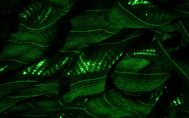 Karmaşık dokuları ve parlak gölgeleri olan yeşil bir kumaşın bulanıklığı. Bileşim, dokuma desenleri ve parlayan ipliklere odaklanarak dokuların ve ışığın dinamik kontrastını oluşturur..