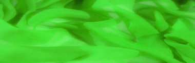 Neon yeşil şifon kumaştan bulanık, yumuşak bükülmüş ve örtülmüş. Hafif kumaş pürüzsüz dokuları vurgular, katların pürüzsüz akışı zarif kıvrımlar oluşturur.