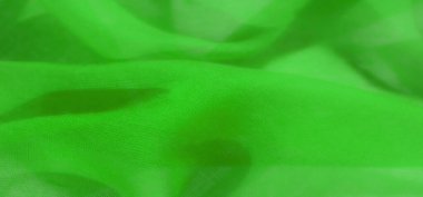 Parlak yeşil kumaşlar yavaşça kıvrılarak akışkan şekillere dönüşür. Saf malzemeler yumuşak kıvrımlar ışığı yakalar, parlak ve zarif bir örtü etkisi yaratır..