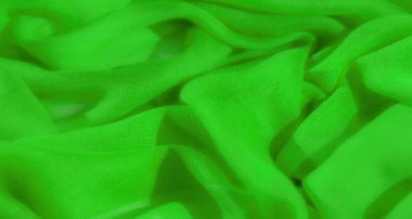 Parlak yeşil kumaş bulanıklığı, ince kıvrımlarla karışık. Kumaşın ince dokusu ışığı yakalar ve yüzeyde yumuşak gölgeler oluşturur..