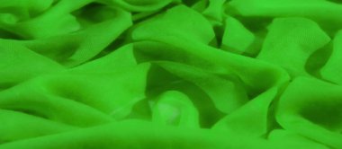 Saf yeşil kumaştan bulanık. Yumuşak kıvrımları akışkan bir dizaynla sıralanmış. Malzemenin ince dokusu ışığı yakalar, parlak ışıklar ve ince gölgeler yaratır..