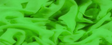 Canlı yeşil bir tekstil bulanıklığı, yumuşak spirallerde sıkıca toplanmış. Kumaşların şeffaf doğası ışığın içinden geçmesine izin veriyor, pürüzsüz dokusu ve dinamik akışını vurguluyor..