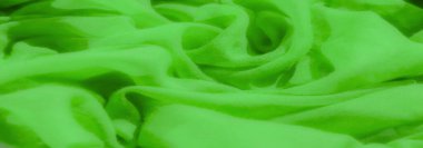 Pürüzsüz, dalgalı bir dokusu olan parlak yeşil kumaş bulanıklığı yumuşak ve akıcı bir görünüm yaratıyor. Kumaş kıvrımları ışığı yakalıyor, dokuyu ve parıltıyı vurguluyor..