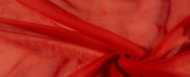 Bulanık kırmızı kumaş ince düğümlerle güzelce örülmüş, yumuşak ışıkta gölgeler bırakıyor. Malzeme dokusu ışıkla oynayarak şeffaflık ve opaklık arasında bir tezat yaratır..