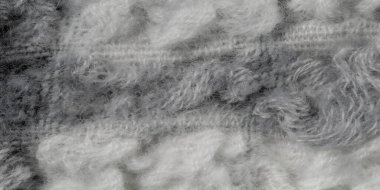 Bulanık kumaş dokusunda gri ve beyaz tonlarda kabarık desenler var. Yumuşak yün kumaş sanatsal olarak dokunmuş, tekstil yüzeyinin rahat ve katmanlı doğasını sergiliyor..