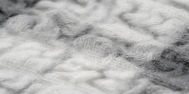 Açık ve koyu tonlarda kabarık desenleri olan, dokuma dokusunun bulanık yakın çekimi, karmaşık bir dokuma sergiliyor. Yumuşak madde gri ve beyaz renkleri harmanlıyor, ince ve sıcak bir his yaratıyor..