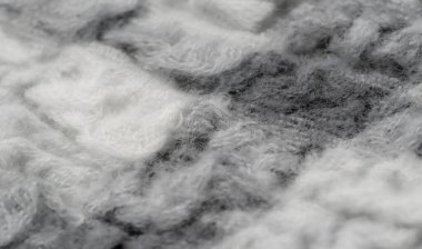 Gri ve beyaz tonların karışımında, yumuşak ve kabarık desenli bulanık kumaş. Materyalin karmaşık dokuması katmanlı sıcak bir his veriyor.