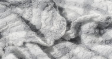 Yumuşak, kabarık beyaz ve gri liflerle örülmüş bir kumaşın bulanıklığı. Dokunsal doku karmaşık dokuma yoluyla vurgulanır ve tekstil odaklı görseller için sıcak ve samimi bir tasarım sağlar..