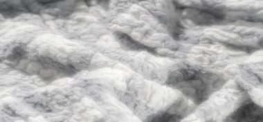 Beyaz ve gri renklerin karışımı yumuşak desenli bulanık bir kumaş. Karmaşık örgü ve lif ayrıntıları rahatlatıcı, nötr bir görsel yaratıyor, tekstil tasarımı ve ev dekorasyonu için ideal.