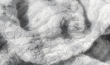 Bulanık gri tonlu ve kabarık, desenli yüzeyi olan beyaz kumaş. Karmaşık örgü yumuşak, sıcak ve narin bir his yaratıyor, rahat ortamlar ve tekstil tasarımı için mükemmel.