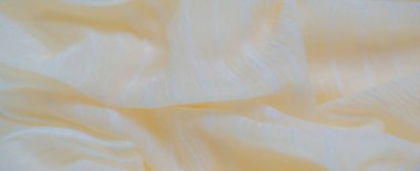 Karmaşık beyaz ipliklerle kaplı bulanık pastel sarı kumaş desenli yüzeyi boyunca sıralanmış. Kumaşın narin pliseleri yumuşak, pürüzsüz bir akış yaratır ve ışık ipliklerini tamamlar.