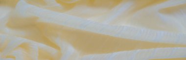 Üst üste binen kıvrımlarda ince çizgili bulanık sarı kumaş. Dokulu yüzey ışığı yakalar ve narin maddenin içinde yumuşak, ışıl ışıl bir parıltı yaratır..