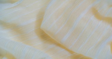 Hassas bir şeffaflık ve parıldayan ipliklerle yüzeye doğru akan yumuşak sarı bir kumaş, narin ve parlak bir doku yaratıyor. Hafif kumaş pürüzsüz görünüyor.