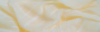 Yumuşak sarı kumaştan bulanık, sıvı kıvrımlı parlak beyaz ipliklerle kompozisyonda zikzak çiziyor. Kumaş ve ipliğin birleşimi soyut ama uyumlu bir görsel yaratıyor..
