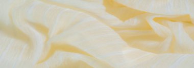 Yumuşak, yumuşak sarı kumaştan bulanık kıvrımlı, beyaz iç içe geçmiş ipliklerle aksanlı. Görüntü, sıcaklığı ve zarafeti akış çizgilerinde ve ince ışıkta anımsatıyor..