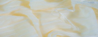 Yumuşak, yumuşak sarı kumaştan bulanık kıvrımlı, beyaz iç içe geçmiş ipliklerle aksanlı. Görüntü, sıcaklığı ve zarafeti akış çizgilerinde ve ince ışıkta anımsatıyor..