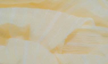 Yumuşak, ışıldayan bir dokusu olan bulanık pastel sarısı kumaş şeffaf ipliklerle sarmalanmış, karmaşık ve narin bir görünüm yaratıyor. Kumaş kıvrımları pürüzsüz ve hafif bir etki yaratıyor.