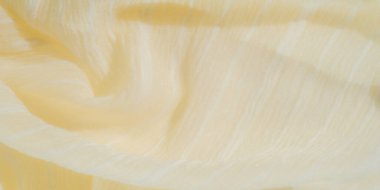 Yumuşak, ışıldayan bir dokusu olan bulanık pastel sarısı kumaş şeffaf ipliklerle sarmalanmış, karmaşık ve narin bir görünüm yaratıyor. Kumaş kıvrımları pürüzsüz ve hafif bir etki yaratıyor.