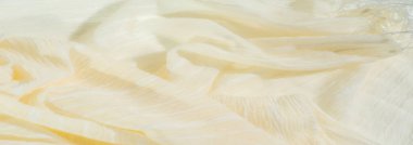 Yumuşak, akışkan sarı kumaştan oluşan bulanık, şeffaf ipliklerle vurgulanmış, karmaşık, katmanlı bir desen oluşturuyor. Yumuşak dokular ve parıldayan ipliklerin birleşimi ona lüks ve modern bir his veriyor.