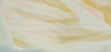 Yumuşak, ışıldayan bir dokusu olan bulanık pastel sarısı kumaş şeffaf ipliklerle sarmalanmış, karmaşık ve narin bir görünüm yaratıyor. Kumaş kıvrımları pürüzsüz ve hafif bir etki yaratıyor.