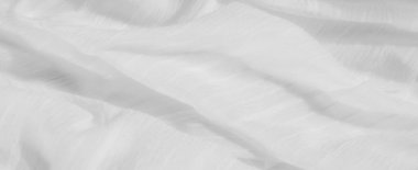 Hafif beyaz kumaş bulanıklığı yumuşak, dalgalı çizgiler ve sakin bir doku oluşturuyor. Katlar ve kırışıklıklar kumaşa soyut, minimalist bir görünüm verir ve saflığı vurgular.