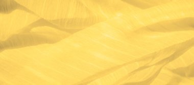 Bulanık sarı kumaş dalgalanma etkisiyle hassas kıvrımlar oluşturarak hareket hissi uyandırıyor. Saf doku ve sıcak ton görüntüye hafif ve havadar bir his verir.
