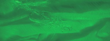 Yumuşak kıvrımlara dolanmış parlak iplikleri olan yeşil kumaş bulanıklığı. Parlak doku ve soyut ışık enerjik ve dinamik bir desen yaratır..
