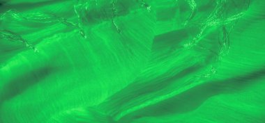 Bulanık yeşil kumaş, akıcı dokular ve ince iplik aksanlarıyla hareket ve yumuşaklık hissi yaratıyor. Parlak iplikler parıldayan bir detay ekler..