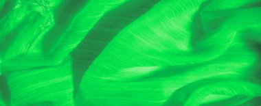 Dokuları kıvrımlı parlak yeşil kumaş bulanıklığı soyut ve akışkan bir etki yaratıyor. Pürüzsüz yüzeyden yansıyan ışık, kumaşın dinamik hareketini arttırır..