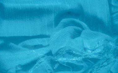 Pürüzsüz mavi kumaş, hafif kırışıklıklar yumuşak, akışkan bir doku yaratıyor. Kumaş narin çizgiler ve ince kıvrımlar sergiliyor..