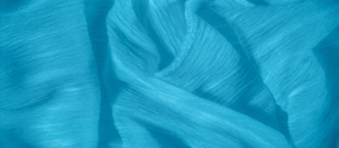 Bulanık, yumuşak mavi kumaş zarif bir şekilde karmaşık kıvrımlarla örtülmüş, sakin ve zarif bir doku yaratıyor. Pürüzsüz yüzeydeki ışık etkileşimi akıcılığını vurgular.,