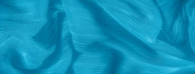 Pürüzsüz mavi kumaş, hafif kırışıklıklar yumuşak, akışkan bir doku yaratıyor. Kumaş narin çizgiler ve ince kıvrımlar sergiliyor..