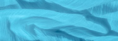 Pürüzsüz mavi kumaşlı, dalgalı bir bulanıklık. Kumaşın ipeksi yüzeyi, yumuşak kıvrımlar ve dokulu bir görünüm ile sakin ve sakinleştirici bir etki yaratıyor..