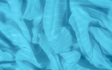Mavi kumaş bulanıklığı ince dokular ve kıvrımlar sergiliyor, hafif bir ışık ve gölge oyunu yaratıyor. Malzemenin yumuşak kırışıklıkları ve hareketleri dinamik ve akışkan bir hissi uyandırıyor..