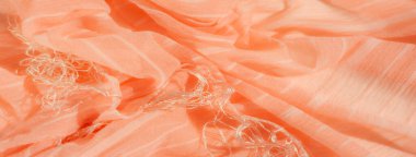 Yumuşak, akıcı şeftali renginde ince beyaz çizgili bir kumaş pürüzsüz, dokulu bir yüzey yaratır. Nazik kıvrımlar maddeye derinlik ve hareket hissi katar..