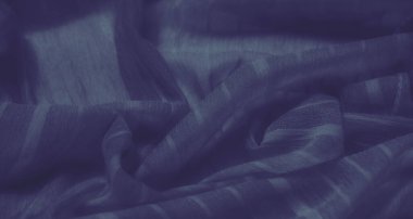 Yumuşak çizgileri ve kıvrımları olan pürüzsüz mavi kumaş gölgelerin ve ışığın yumuşak yüzeydeki hassas etkileşimini yakalıyor. Yapılı ve akışkan