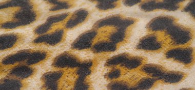Görüntü, canlı leopar desenli kumaş, sarı, siyah ve bej renklerin karışımı. Kumaş kırışık ve dokulu, desene derinlik ve boyut ekliyor..