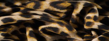 Bulanık, ılık sarı ve siyah leopar desenli kumaş, karmaşık kıvrımları ve lüks dokusuyla, egzotik bir manzaranın vahşi güzelliğini çağrıştırıyor..