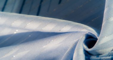 Açık mavi kumaş, şeffaf dalgalar ve ince çizgiler, ışığın ve gölgenin yumuşak etkileşimiyle vurgulanır, dinamik ve zarif bir görsel doku yaratır..