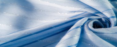 Dalgalı mavi kumaştan ince desenler ve hafif dalgalanmalar. Işığın ve dokunun etkileşimini yakalıyor. Yumuşak ve zarif bir görsel akış yaratıyor..