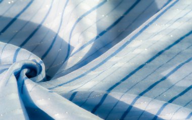 Yumuşak kıvrımları ve ince çizgileri olan açık mavi kumaş, hafif ışık yansımalarıyla aydınlatılıyor, akış ve yumuşaklığın hassas ve rahatlatıcı görsel dokusunu yaratıyor..