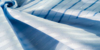 Yumuşak dalgalı, parlak çizgileri olan, güneş ışığıyla aydınlatılan soyut mavi kumaş. Pürüzsüz doku ve ışık yansıması, tasarım için mükemmel, sakin ve akıcı bir etki yaratır..