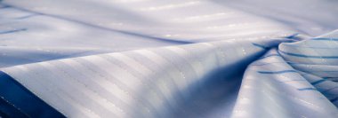 Dalgalı mavi kumaştan ince desenler ve hafif dalgalanmalar. Işığın ve dokunun etkileşimini yakalıyor. Yumuşak ve zarif bir görsel akış yaratıyor..