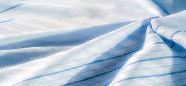 Işıklı bulanık mavi kumaş, parlak iplikler ve mavi tonlardaki yumuşak çizgiler hassas, akıcı bir doku yaratır. Güneş ışığı, yumuşak kıvrımları ve ışıltıyı arttıran nazik bir kontrastı ekler..